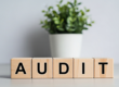 Wooden blocks spelling AUDIT on a white table in a bright office setting symbolizing financial review