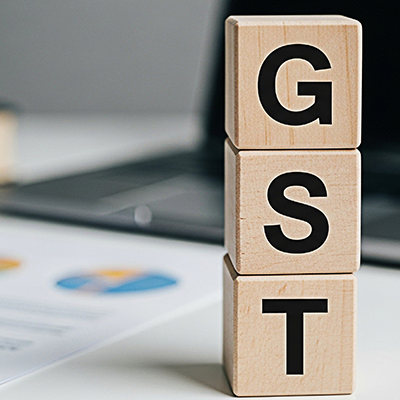 Wooden blocks spelling GST stacked on a white desk with laptop and financial report representing